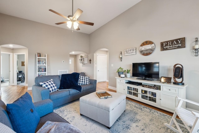 living room featuring ceiling fan, a towering ceiling, and light wood-type flooring