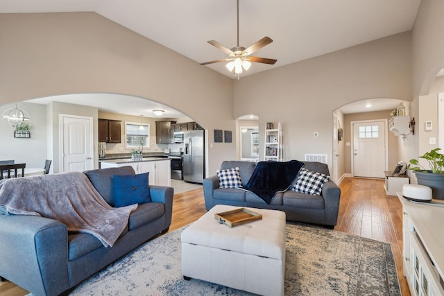 living room featuring light hardwood / wood-style floors, ceiling fan with notable chandelier, and vaulted ceiling