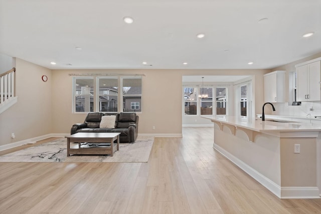 kitchen with a notable chandelier, sink, white cabinetry, and light hardwood / wood-style floors