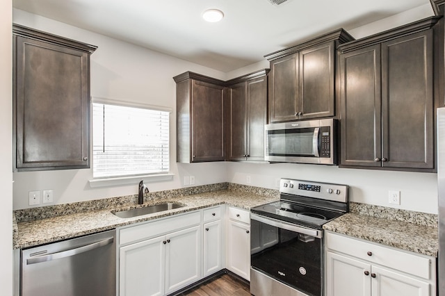 kitchen with stainless steel appliances, dark hardwood / wood-style flooring, white cabinets, light stone counters, and sink