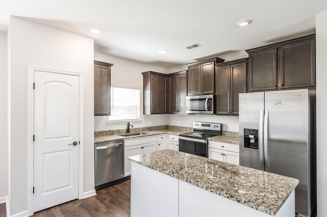 kitchen with appliances with stainless steel finishes, a center island, sink, dark hardwood / wood-style floors, and light stone counters