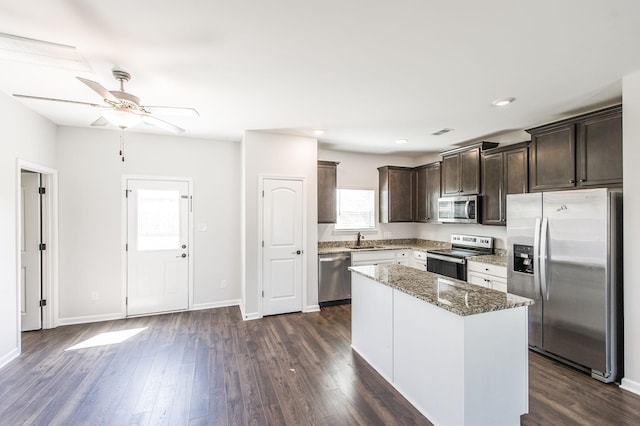 kitchen featuring light stone countertops, appliances with stainless steel finishes, a center island, dark wood-type flooring, and sink