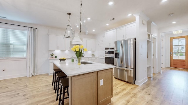 kitchen with pendant lighting, white cabinetry, stainless steel appliances, and an island with sink