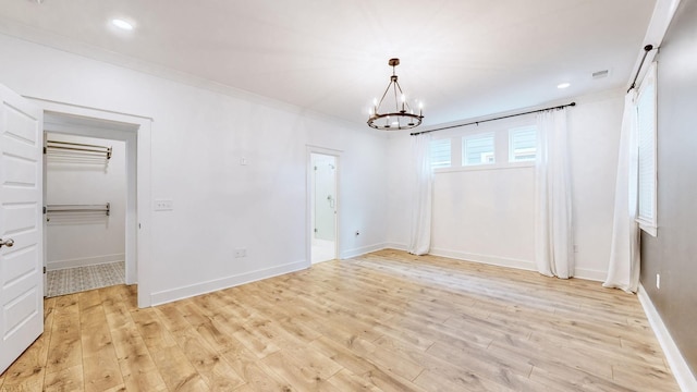 spare room featuring light hardwood / wood-style flooring, crown molding, and a chandelier