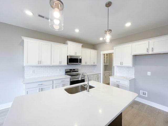 kitchen with white cabinets, decorative light fixtures, stainless steel appliances, tasteful backsplash, and a center island with sink