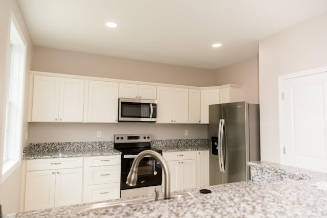 kitchen with white cabinetry, a wealth of natural light, light stone countertops, and appliances with stainless steel finishes