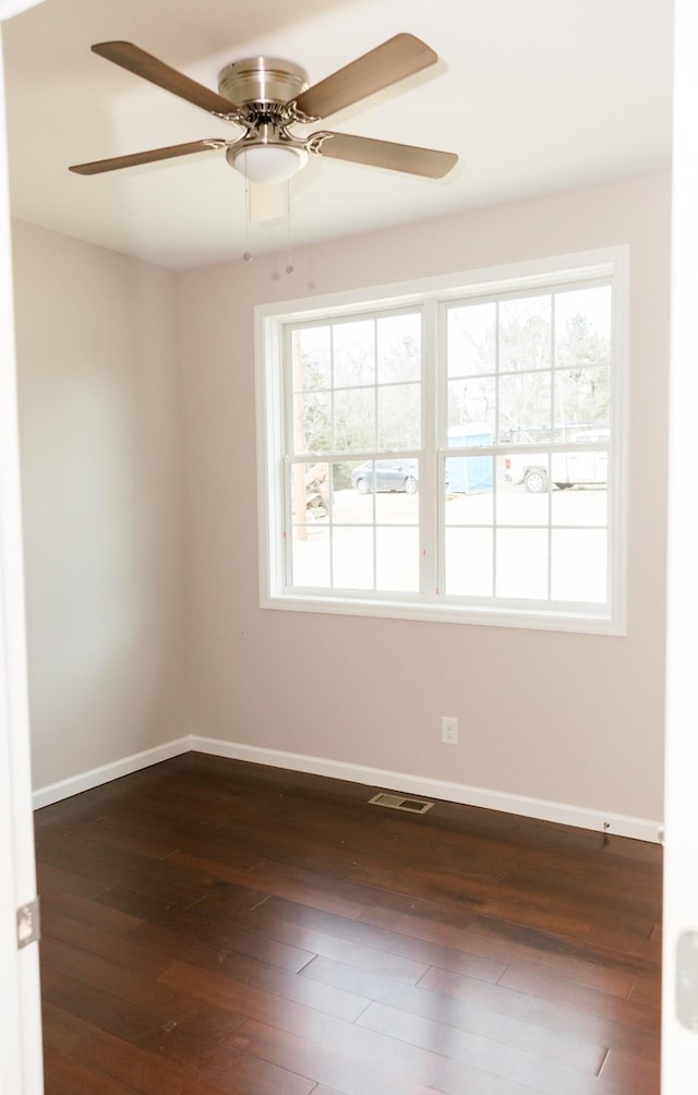 spare room featuring visible vents, plenty of natural light, baseboards, and dark wood-style floors