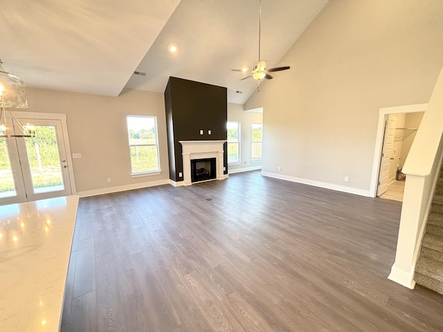 unfurnished living room featuring high vaulted ceiling, a wealth of natural light, dark hardwood / wood-style flooring, and ceiling fan with notable chandelier