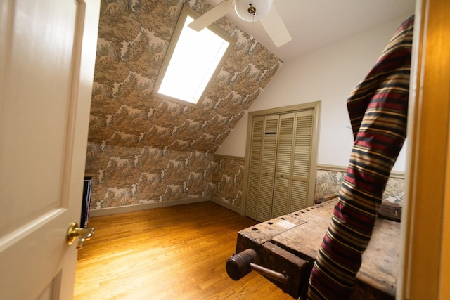 additional living space featuring light wood-type flooring, ceiling fan, and lofted ceiling with skylight