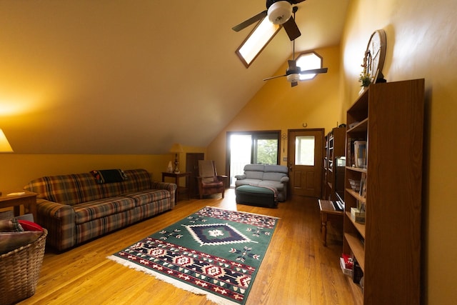 living room featuring ceiling fan, vaulted ceiling with skylight, and wood-type flooring