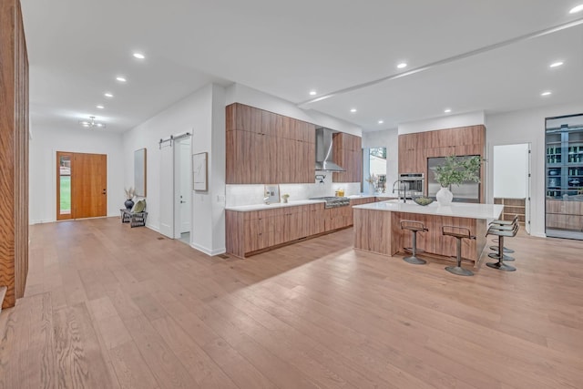 kitchen with a barn door, wall chimney exhaust hood, modern cabinets, stainless steel appliances, and light countertops