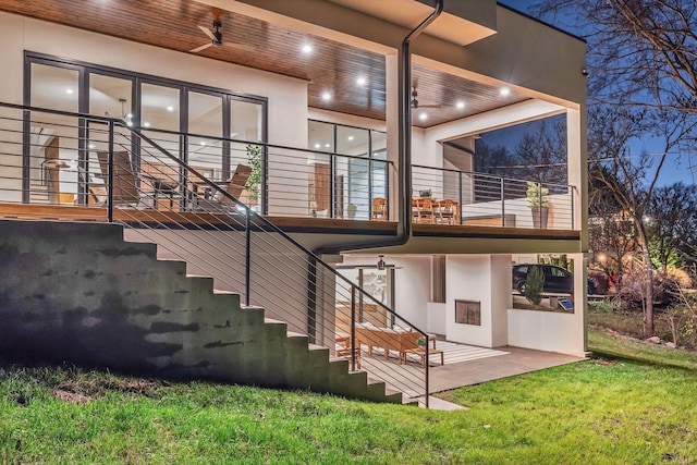 rear view of property featuring a yard, stairway, a balcony, and stucco siding