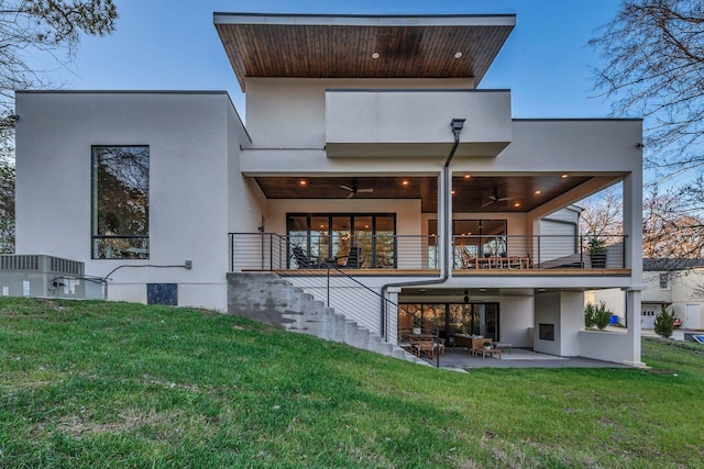 rear view of property featuring a patio, a lawn, a balcony, and stucco siding