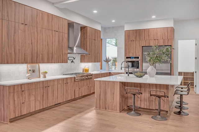 kitchen with stainless steel appliances, wall chimney range hood, modern cabinets, and a kitchen breakfast bar