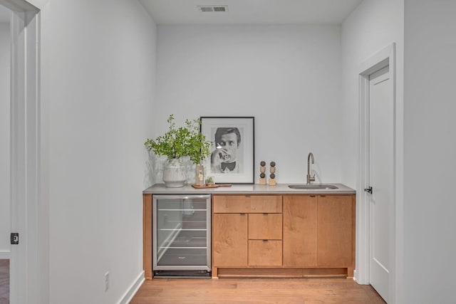 bar with light wood finished floors, wine cooler, visible vents, and a sink