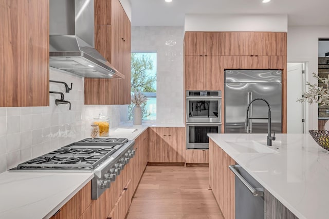 kitchen with wall chimney exhaust hood, appliances with stainless steel finishes, modern cabinets, and light stone countertops