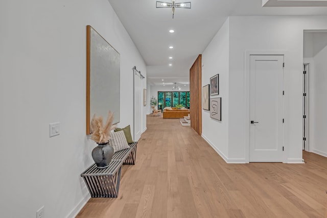 hall featuring light wood-type flooring, baseboards, recessed lighting, and a barn door