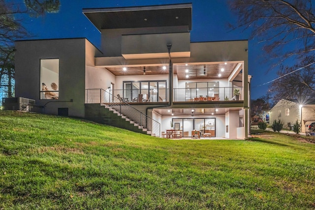 rear view of property featuring a yard, a patio, stucco siding, a balcony, and stairs