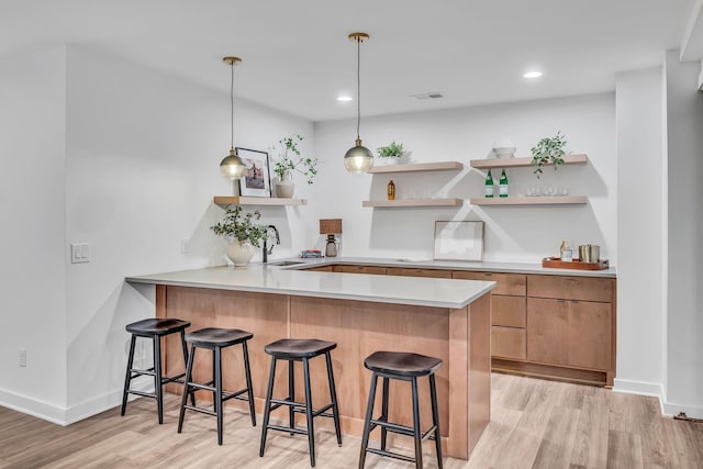 kitchen featuring light wood-style floors, a breakfast bar area, open shelves, and a sink