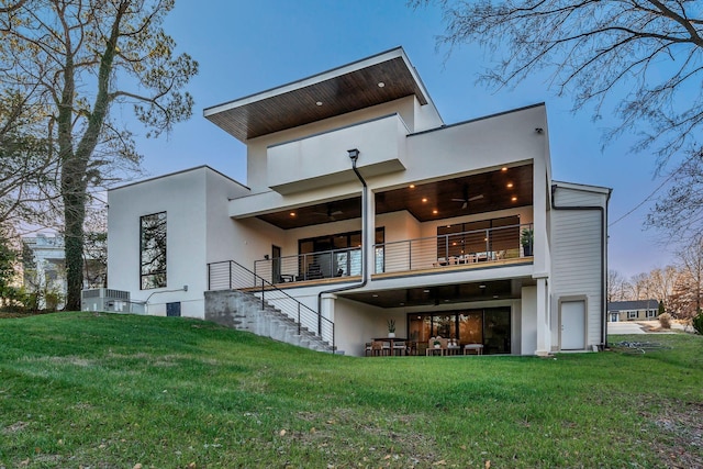 rear view of house featuring a yard, stairway, a balcony, and stucco siding