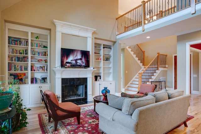 living room with built in shelves, light wood-type flooring, a towering ceiling, and a tile fireplace