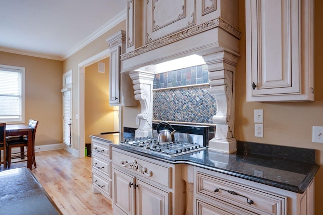 kitchen featuring stainless steel gas stovetop, decorative backsplash, dark stone counters, crown molding, and light hardwood / wood-style flooring