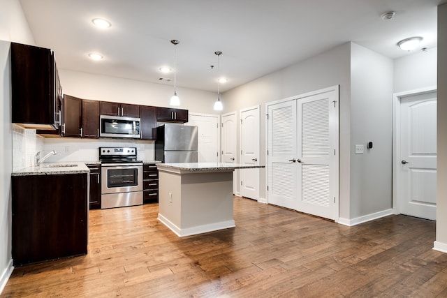 kitchen with stainless steel appliances, decorative light fixtures, dark brown cabinets, a kitchen island, and sink