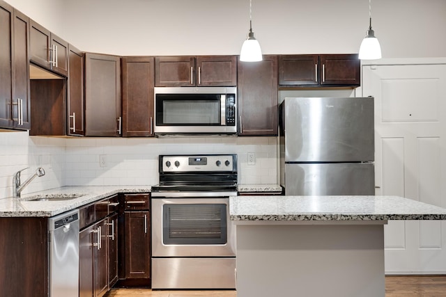 kitchen with stainless steel appliances, pendant lighting, light stone counters, and sink