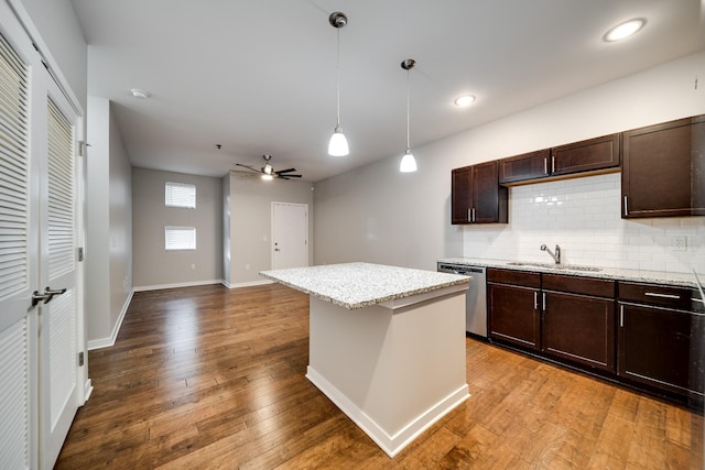 kitchen featuring tasteful backsplash, decorative light fixtures, stainless steel dishwasher, light stone counters, and a center island