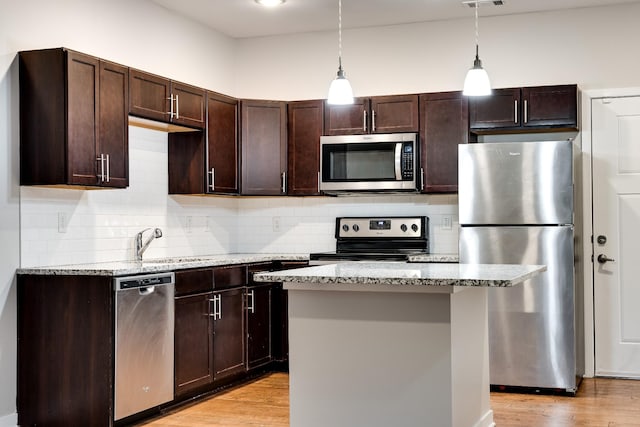 kitchen with light stone countertops, pendant lighting, appliances with stainless steel finishes, and a center island