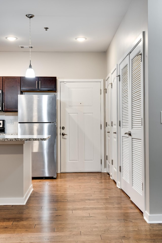 kitchen with stainless steel appliances, decorative backsplash, pendant lighting, light stone counters, and dark brown cabinetry