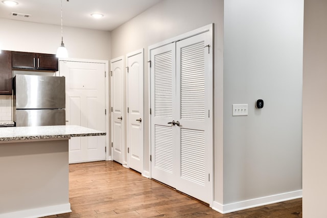 kitchen featuring decorative light fixtures, light hardwood / wood-style floors, stainless steel refrigerator, light stone counters, and dark brown cabinets