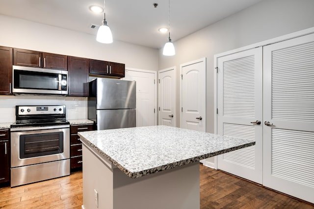 kitchen featuring pendant lighting, dark brown cabinetry, a kitchen island, stainless steel appliances, and backsplash