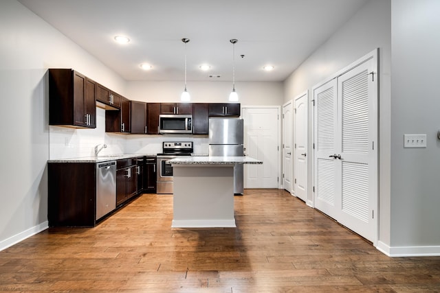 kitchen with pendant lighting, a kitchen island, stainless steel appliances, sink, and light hardwood / wood-style flooring