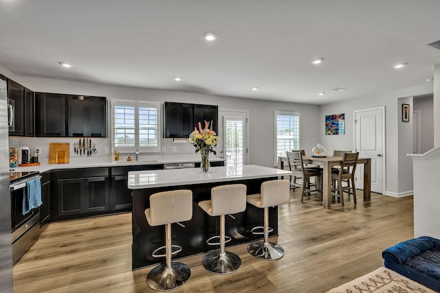 kitchen featuring a kitchen island, a kitchen bar, sink, stainless steel range with electric stovetop, and light hardwood / wood-style flooring