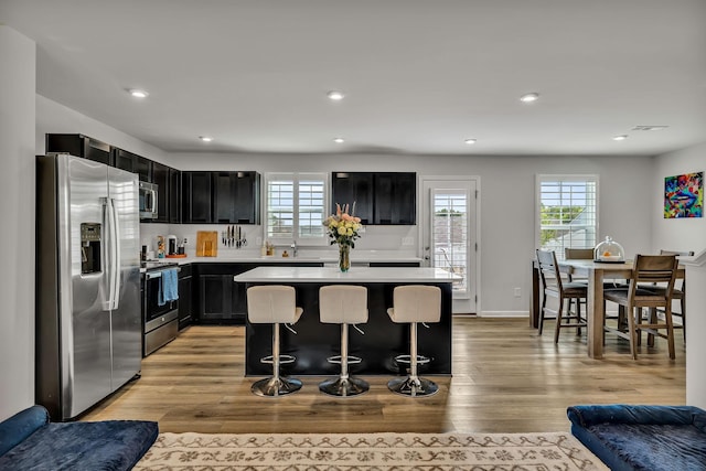 kitchen with appliances with stainless steel finishes, a kitchen island, light hardwood / wood-style flooring, a breakfast bar, and sink