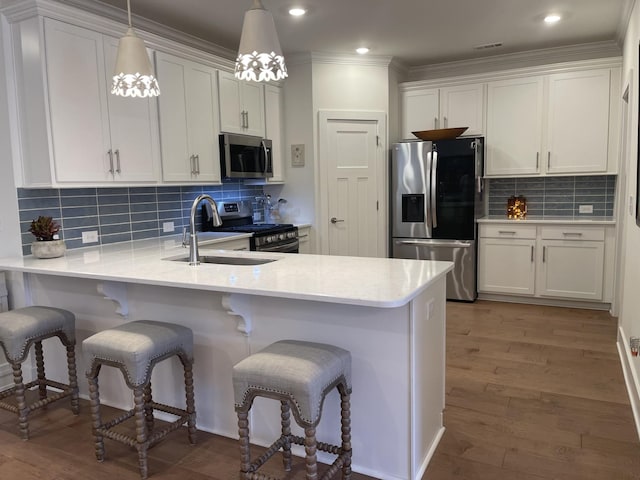 kitchen featuring appliances with stainless steel finishes, hanging light fixtures, white cabinets, a breakfast bar, and sink