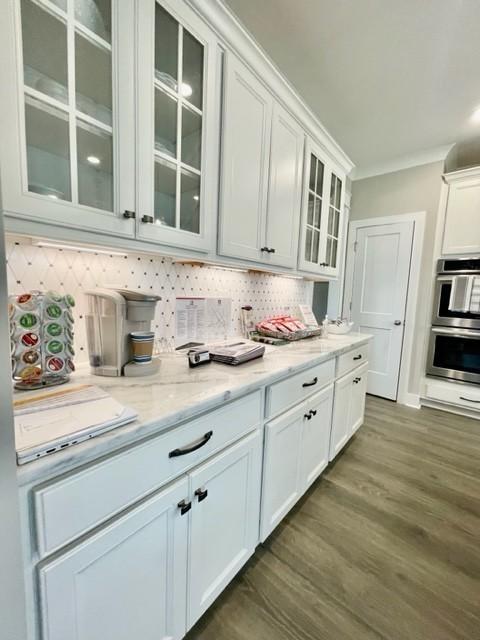 kitchen with stainless steel double oven, decorative backsplash, white cabinets, dark hardwood / wood-style flooring, and light stone counters