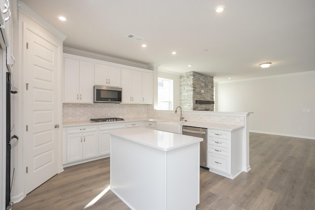 kitchen with white cabinets, appliances with stainless steel finishes, a center island, sink, and light wood-type flooring