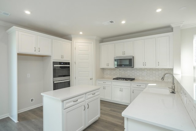 kitchen featuring appliances with stainless steel finishes, a center island, white cabinetry, tasteful backsplash, and sink