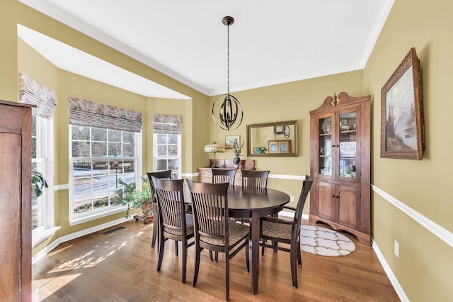 dining space with ornamental molding, wood-type flooring, and a notable chandelier