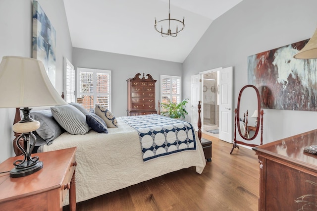 bedroom with hardwood / wood-style floors, lofted ceiling, ensuite bath, and a chandelier