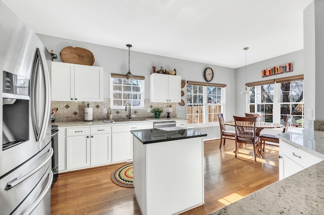 kitchen featuring appliances with stainless steel finishes, tasteful backsplash, hanging light fixtures, light stone countertops, and white cabinets