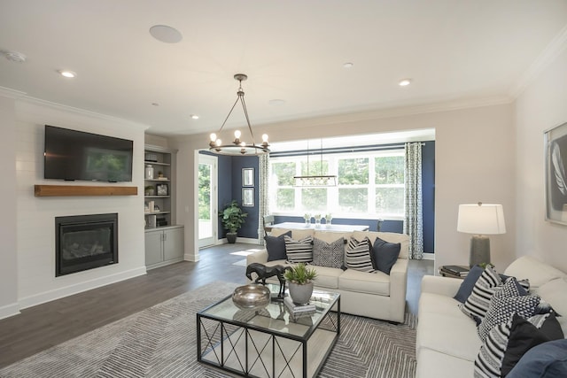 living room with a notable chandelier, dark hardwood / wood-style floors, a large fireplace, crown molding, and built in shelves