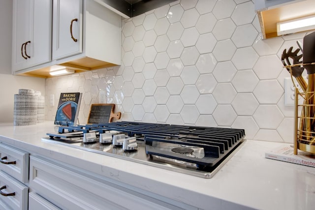 interior details with stainless steel gas stovetop, white cabinetry, and backsplash