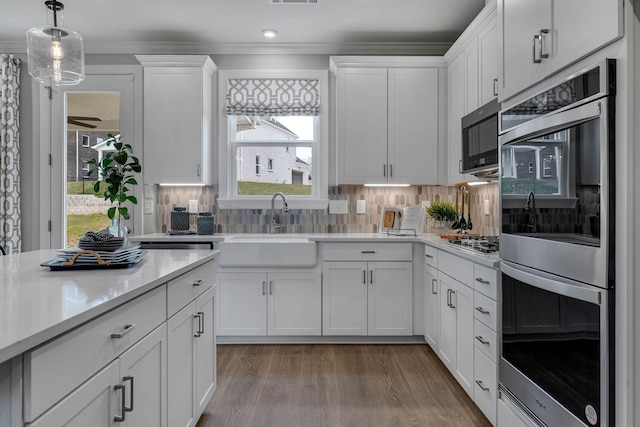 kitchen featuring appliances with stainless steel finishes, decorative light fixtures, white cabinetry, tasteful backsplash, and light hardwood / wood-style floors