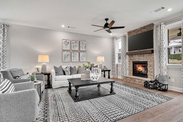 living room featuring ceiling fan, crown molding, hardwood / wood-style floors, and a stone fireplace