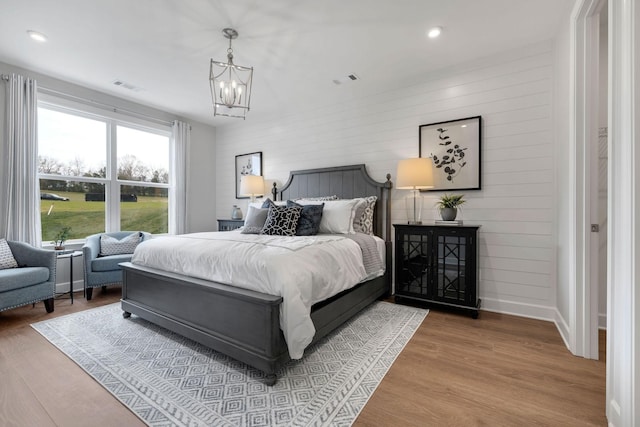 bedroom featuring a notable chandelier, wooden walls, and light hardwood / wood-style floors