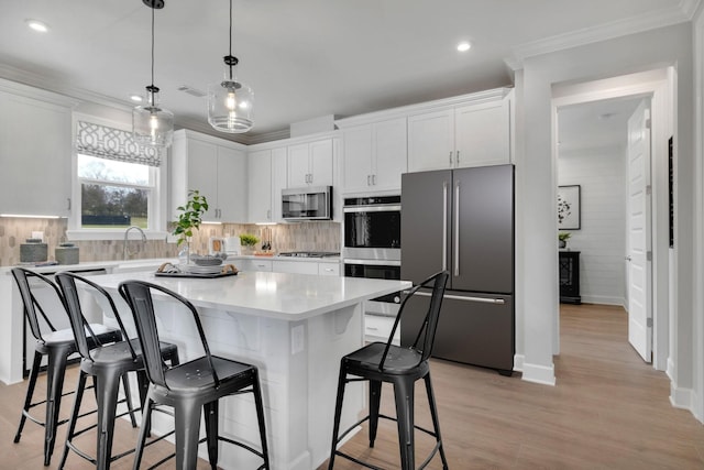 kitchen with stainless steel appliances, white cabinets, decorative light fixtures, and a center island