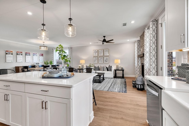 kitchen featuring white cabinets, dishwasher, decorative light fixtures, a stone fireplace, and light hardwood / wood-style flooring